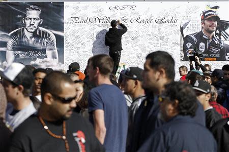 A man signs a large condolence card during an unofficial memorial event for "Fast & Furious" star Paul Walker in Santa Clarita, California December 8, 2013. Thousands of fans are visiting the area near the site where Paul Walker and Roger Rodas died in a single-vehicle accident last weekend. REUTERS/Jonathan Alcorn