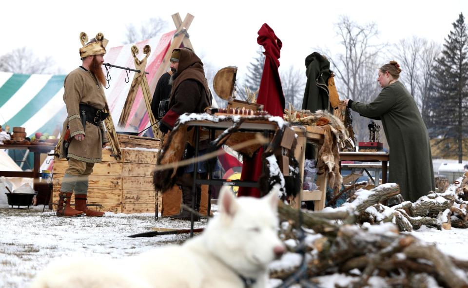 As Star Duster, a 3-year-old Siberian Husky, looks around, members of the Michigan Viking Alliance talk and get items for sale ready in the morning before the opening of the Michigan Nordic Fire Festival at the Eaton County Fairgrounds in Charlotte on Saturday, Feb. 25, 2023.