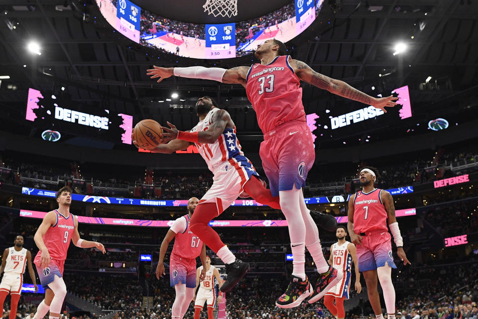 Brooklyn Nets guard Kyrie Irving (11) goes to the basket against Washington Wizards forward Kyle Kuzma (33) during the second half of an NBA basketball game, Monday, Dec. 12, 2022, in Washington. The Nets won 112-100. Kuzma was charged with a foul on the play. (AP Photo/Nick Wass)