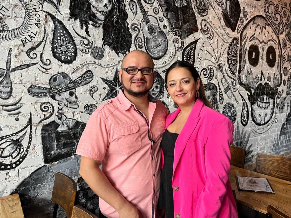 Que Onda owners Manny and Paola Flores stand in front of a first-floor mural by artist Nicole DeSourdy.