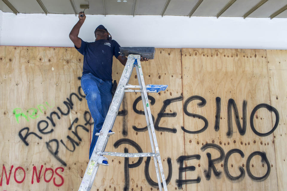 A man paints outside a store that was boarded up to prevent damage amid protests in San Juan, Puerto Rico, Thursday, July 18, 2019. Protesters are demanding Gov. Ricardo Rossello resign after the leak of online chats that show him making misogynistic slurs and mocking his constituents. (AP Photo/Dennis M. Rivera Pichardo)