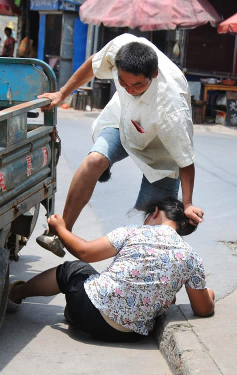 He uses his foot to prevent her from trying to cling to a nearby lorry. (Photo: chinaSMACK.com)