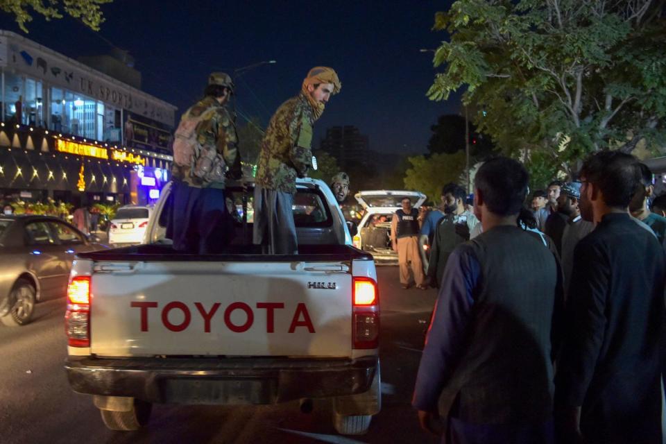 Taliban fighters stand in the bed of a pickup truck outside a hospital as volunteers bring injured people for treatment