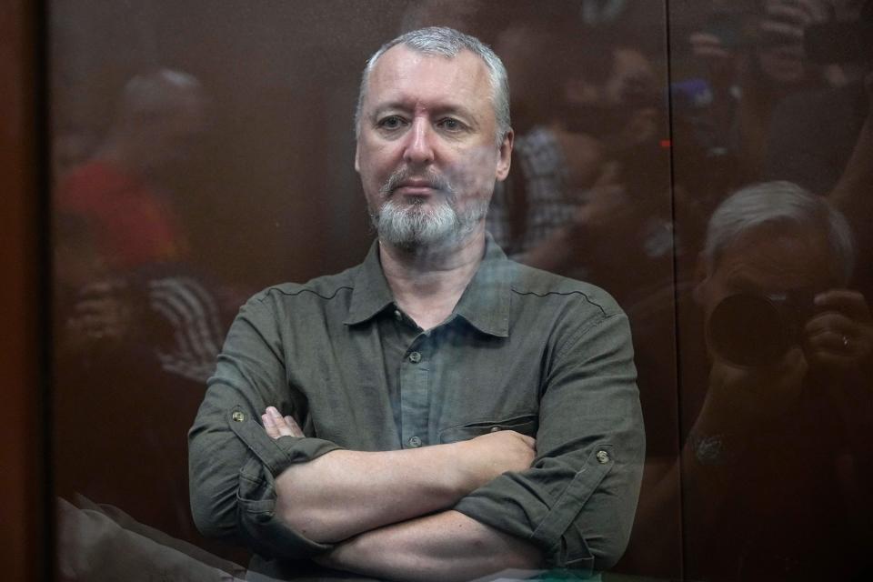 Igor Girkin stands with his arms folded inside a defendant's cage.