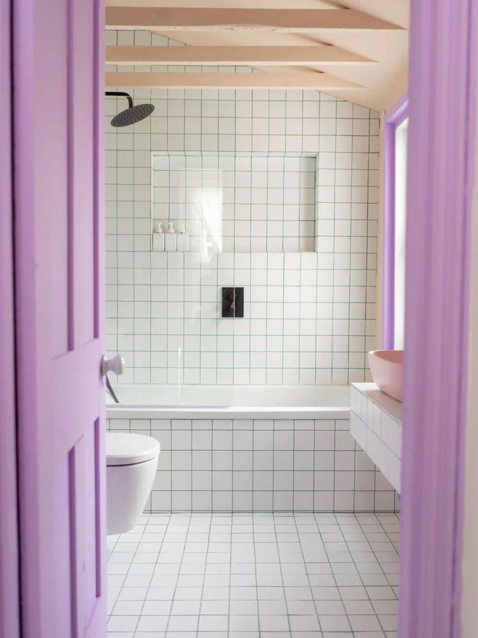 Bathroom with lilac-hued door, white tiles everywhere, and green grout. 