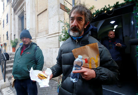 A needy man holds a cheeseburger donated by McDonald's to a charity organization which bestowed them at a walk-in clinic in Rome, Italy January 16, 2017. REUTERS/Tony Gentile