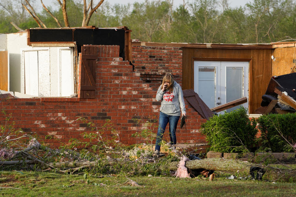 Robbie Bridwell, talking on her cellphone, stands in front of a brick house that has been cracked open.