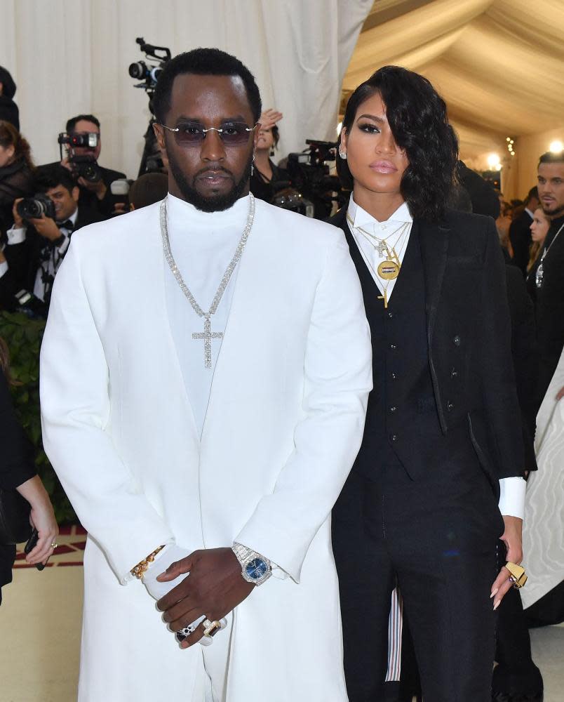 Black man in white suit stands in front of Black woman with long black hair in black suit.