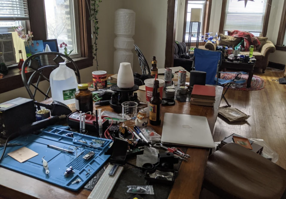 Cluttered table full of electronics and beverages