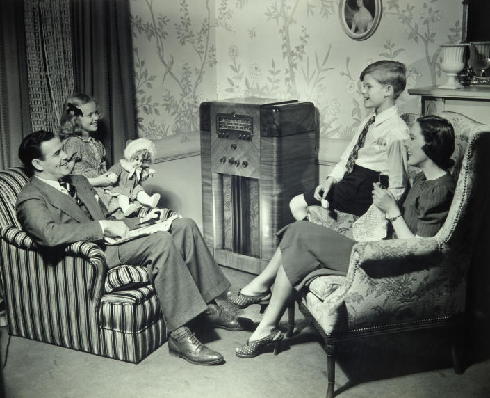 family sitting in living room listening to radio in the 1950s