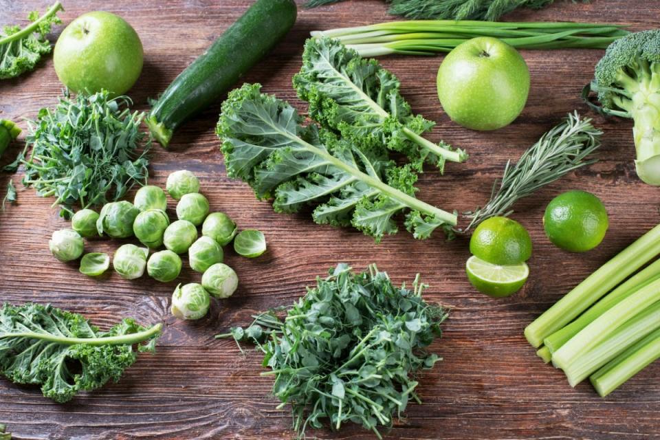 Fresh green vegetables including zucchini, brussels sprouts, and kale on wooden background.