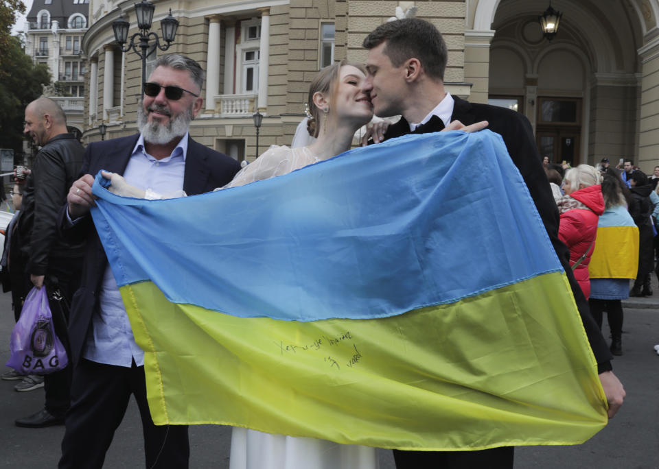 Newly wed Ukrainians hold a Ukrainian flag as people gather in downtown to celebrate the recapturing of Kherson city, Ukraine, Odesa, Saturday, Nov. 12, 2022. People across Ukraine awoke from a night of jubilant celebrating after the Kremlin announced its troops had withdrawn to the other side of the Dnieper River from Kherson, the only regional capital captured by Russia's military during the ongoing invasion. (AP Photo/Nina Lyashonok)