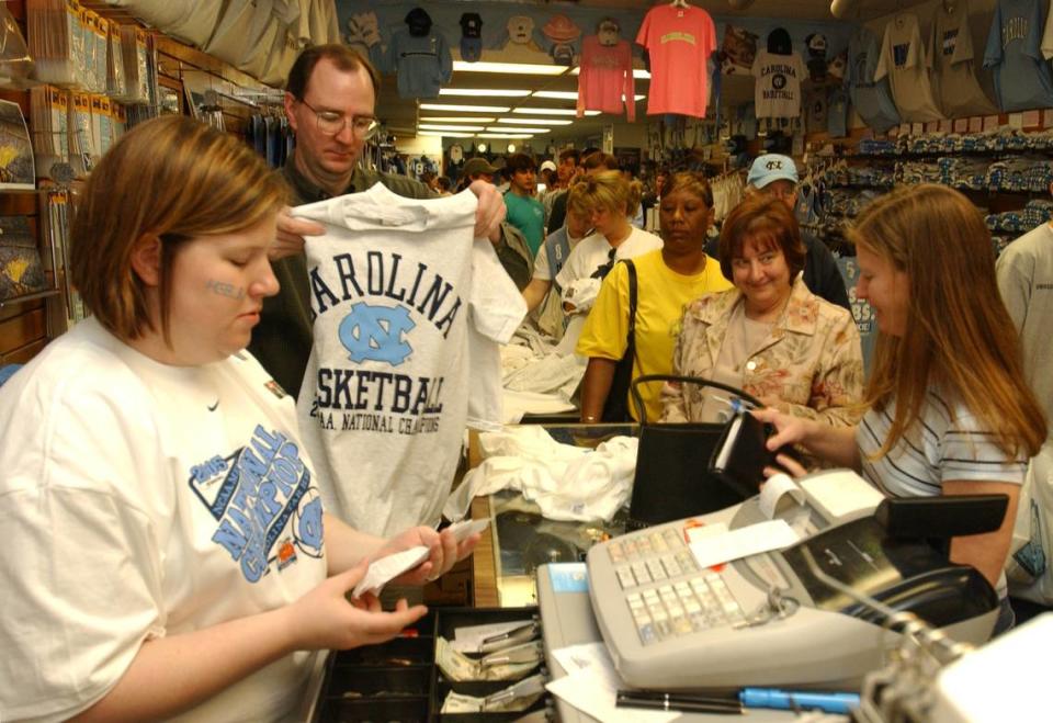 Carolina Pride employee Courtney Lewis, left, works the cash register as Chris Belcher folds another freshly-minted UNC 2005 National Champions tshirt for customer Tracy Jackson of Carrboro, right, during the Tuesday morning crush of shoppers to Franklin Street stores for their NCAA championship t-shirts.