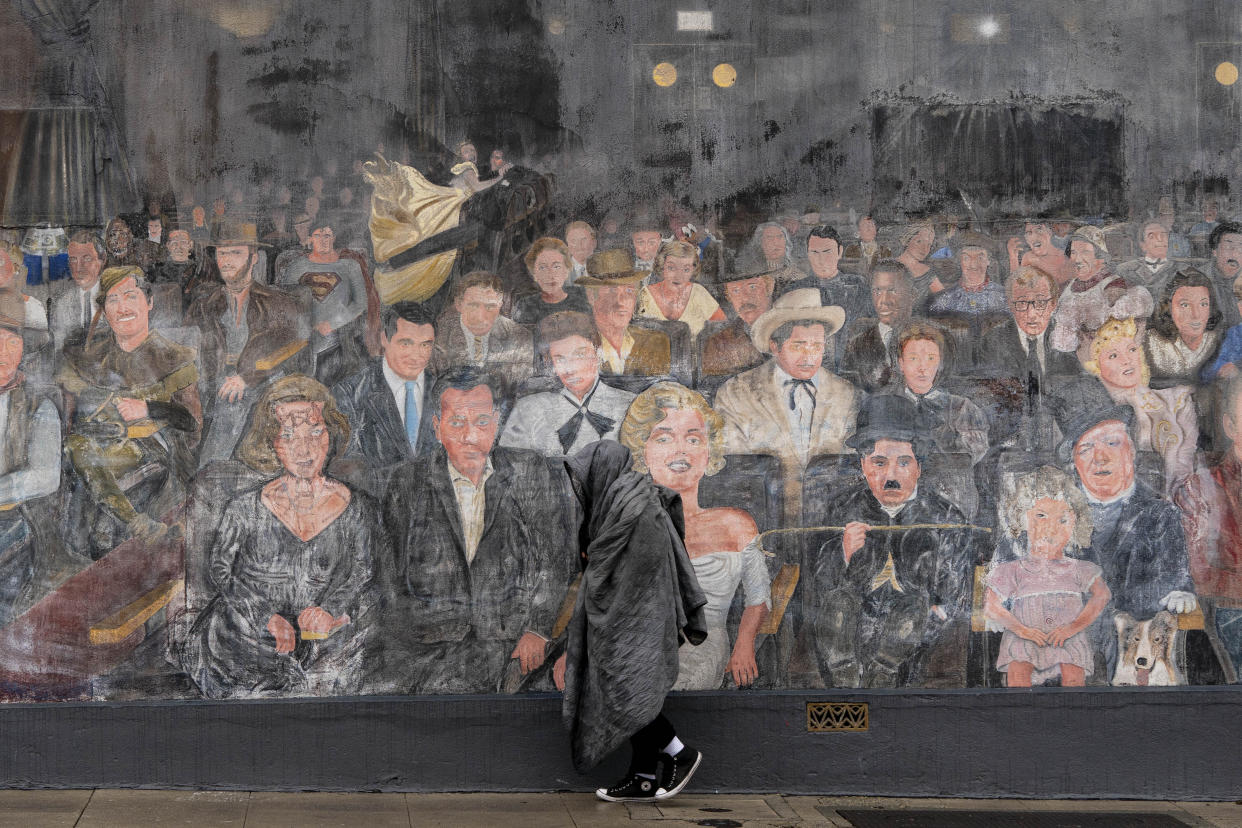 A homeless person with a blanket soaked in rain walks past a mural depicting Hollywood legends in the Hollywood section of Los Angeles, Friday, March 10, 2023. Evacuations were ordered Friday in Northern California after a new atmospheric river brought heavy rain, thunderstorms and strong winds, swelling rivers and creeks and flooding several major highways during the morning commute. (AP Photo/Jae C. Hong)