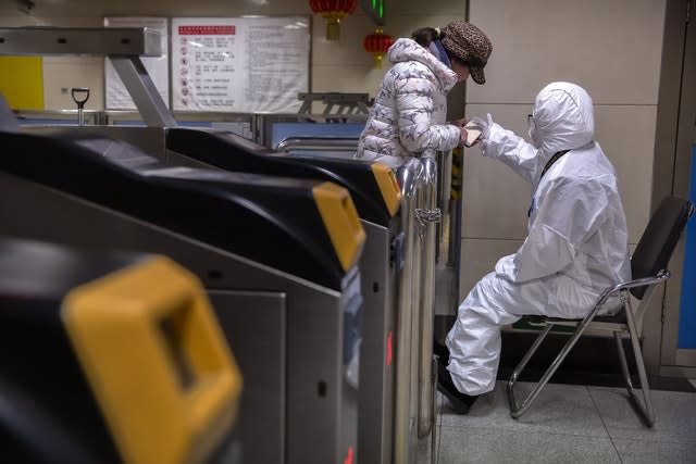 A worker wearing a hazardous materials suit gives directions to a passenger at a subway station in Beijing
