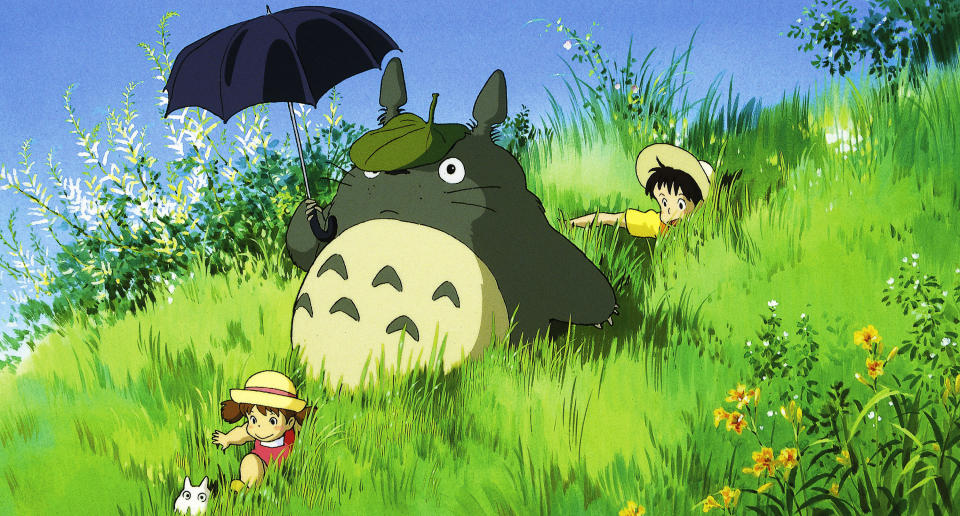 Sisters, Satsuki and Mei going down a grassy hill with Totoro holding his umbrella