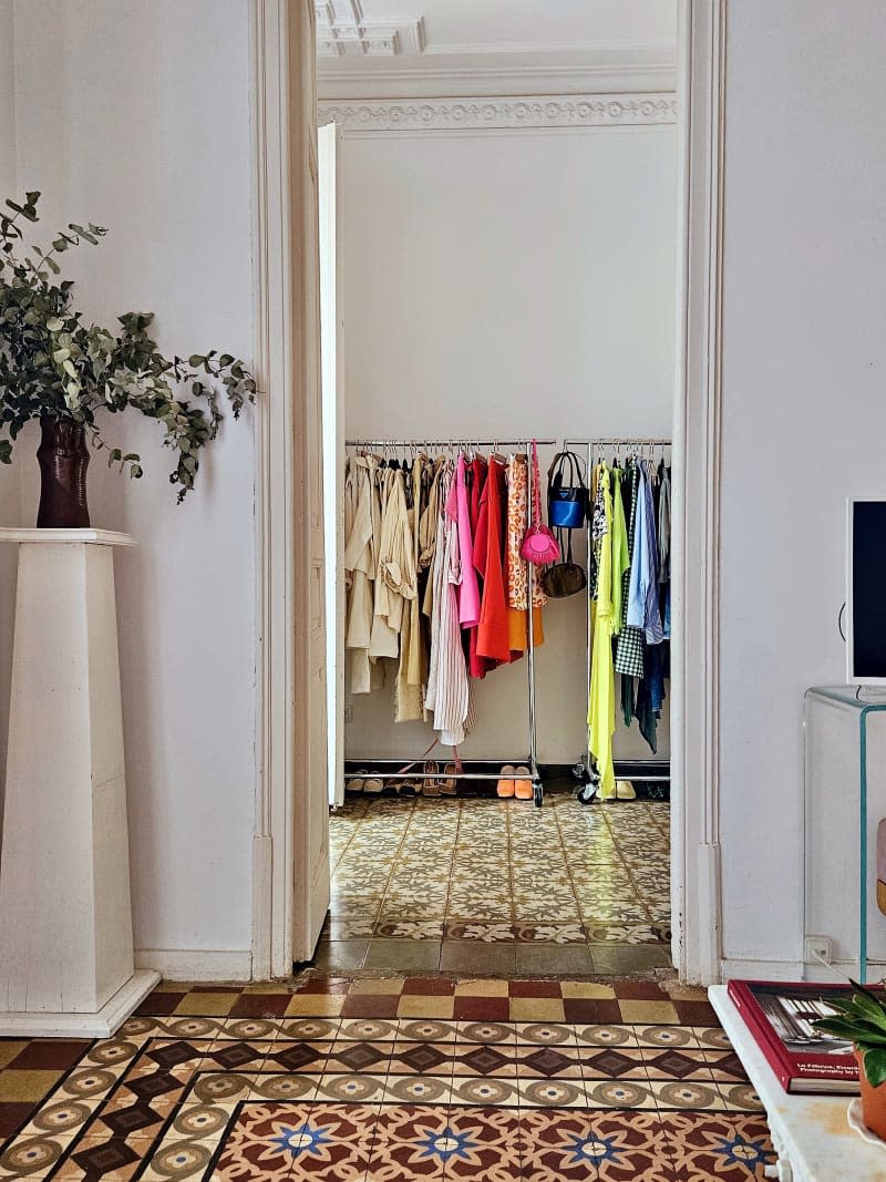 Clothing on a rack in a bedroom with decorated tile floors.