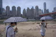 Students carrying umbrellas stand on the dry riverbed of the Jialing River in southwestern China's Chongqing Municipality, Friday, Aug. 19, 2022. Ships crept down the middle of the Yangtze on Friday after the driest summer in six decades left one of the mightiest rivers shrunk to barely half its normal width and set off a scramble to contain damage to a weak economy in a politically sensitive year. (AP Photo/Mark Schiefelbein)