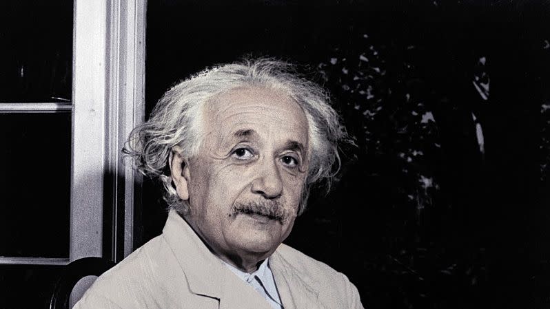 albert einstein sitting by a window and writing on a notepad as he looks up