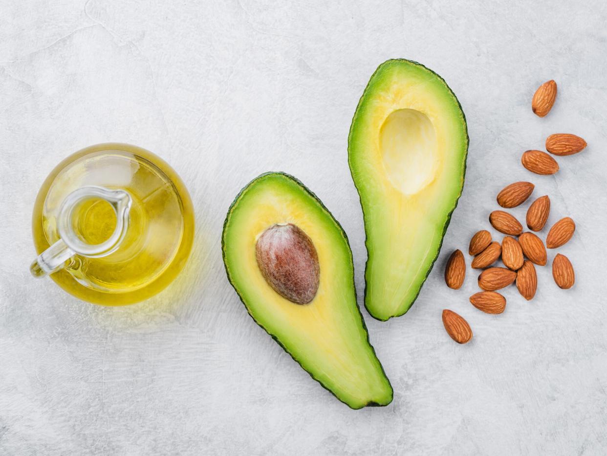 overhead of oil, avocado and almonds on a light grey surface