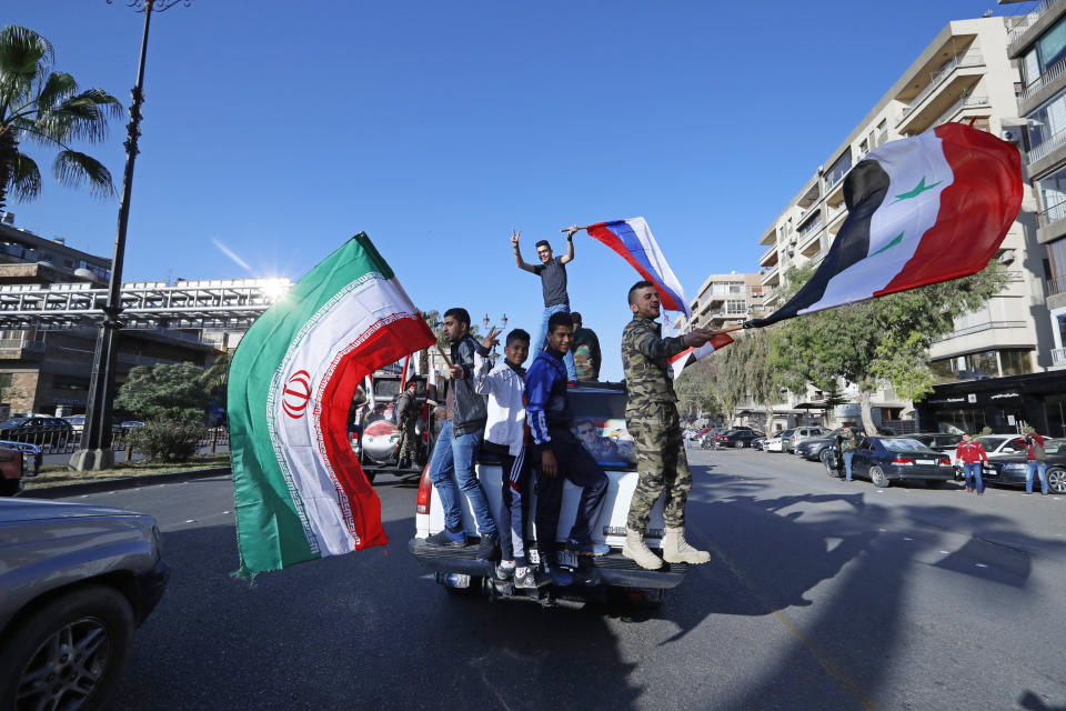 FILE - In this April 14, 2018, file photo, Syrian government supporters wave Syrian, Iranian and Russian flags as they chant slogans against U.S. President Trump during demonstrations following a wave of U.S., British and French military strikes to punish President Bashar Assad for suspected chemical attack against civilians, in Damascus, Syria. n Syria nowadays, there is an impending fear that all doors are closing. After nearly a decade of war, the country is crumbling under the weight of years-long western sanctions, government corruption and infighting, a pandemic and an economic downslide made worse by the financial crisis in Lebanon, Syria's main link with the outside world. (AP Photo/Hassan Ammar, File)
