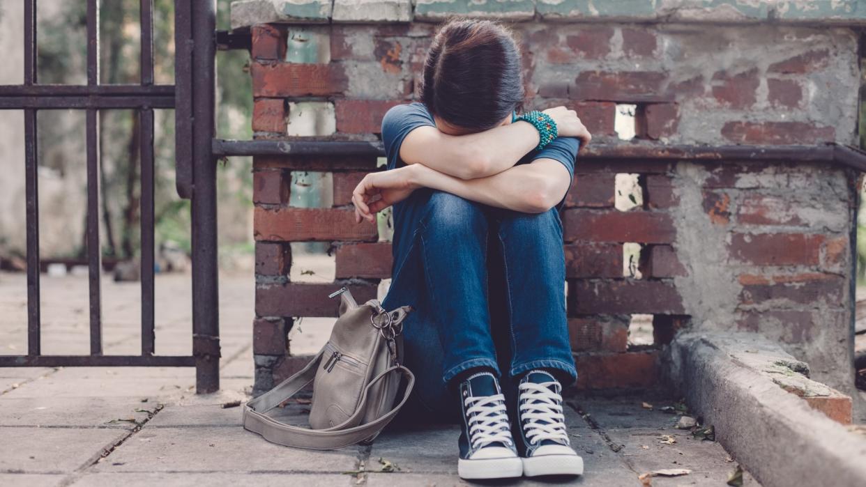 Crying girl with head in hands sitting on the ground.