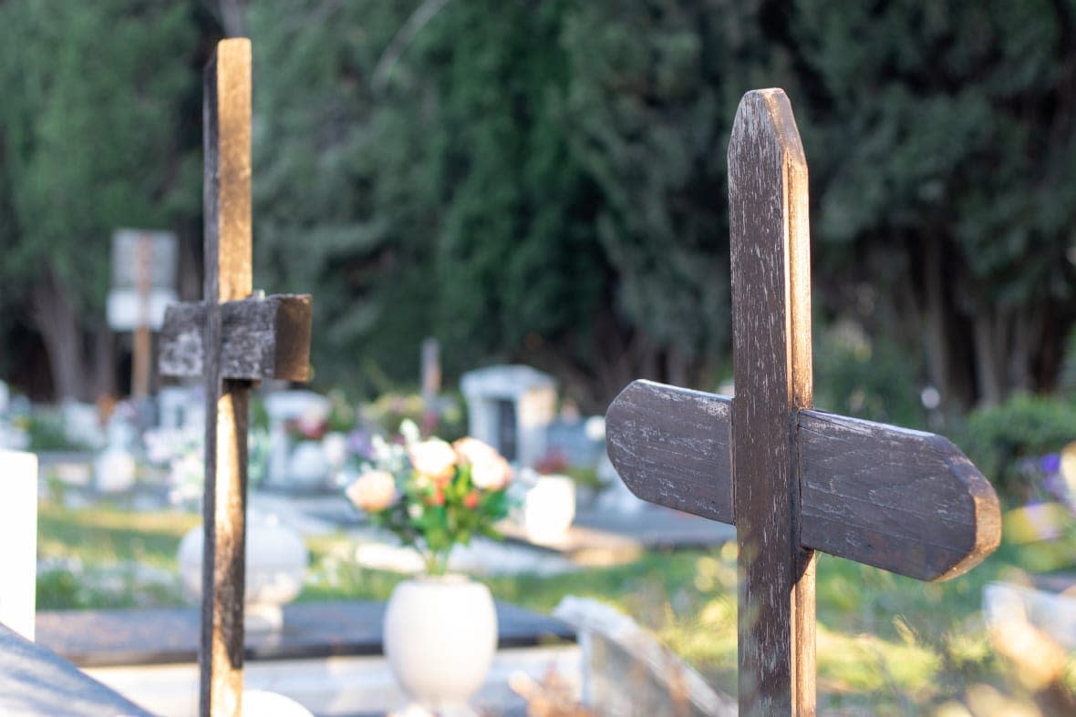 Multiple old brown wooden ruined crosses marking unknown graves in a graveyard. / AdobeStock