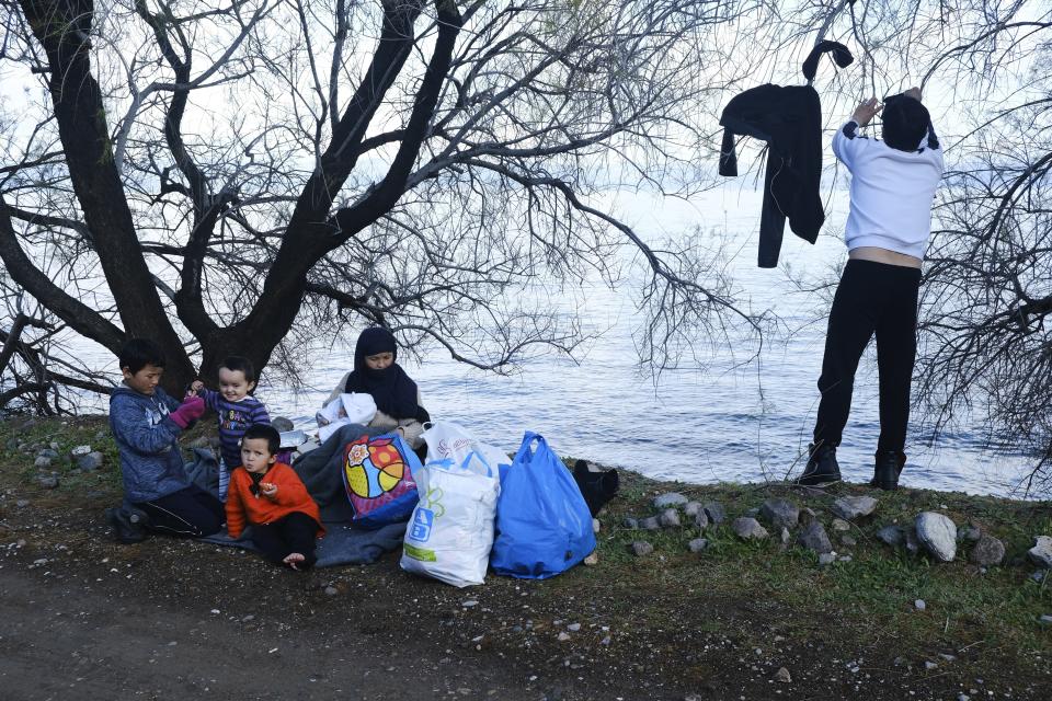 A migrant who arrived yesterday to Greece from Turkey dries his clothes as a family sit under a tree at the village of Skala Sikaminias, on the Greek island of Lesbos on Friday, March 6, 2020. Thousands of refugees and other asylum-seekers have tried to enter Greece from the land and sea in the week since Turkey declared its previously guarded gateways to Europe open. (AP Photo/Alexandros Michailidis)