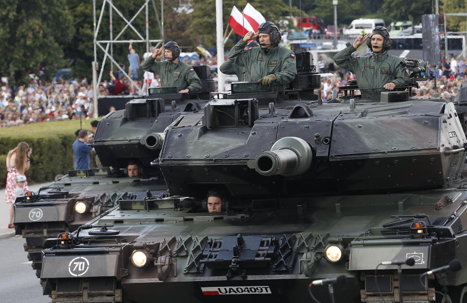 Polish Army soldiers salute as tanks roll on one of the city's main streets during a yearly military parade celebrating the Polish Army Day in Warsaw, Poland, Wednesday, Aug. 15, 2018. Poland marks Army Day with a parade and a call for US permanent military base in Poland.(AP Photo/Czarek Sokolowski)