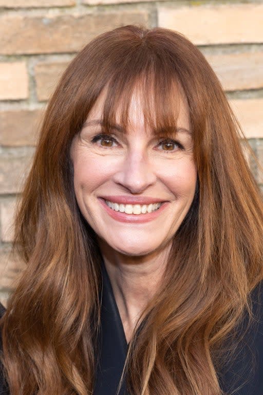 Woman smiling with shoulder-length hair, wearing a v-neck top, against a brick wall