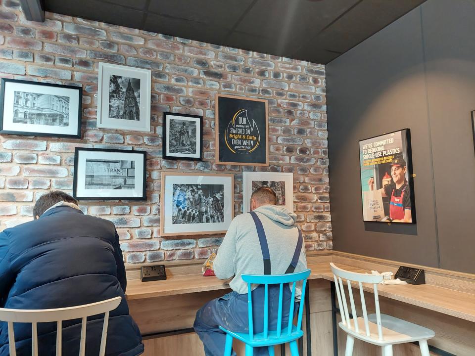 Two men sat on stools by a table at a Greggs store in London