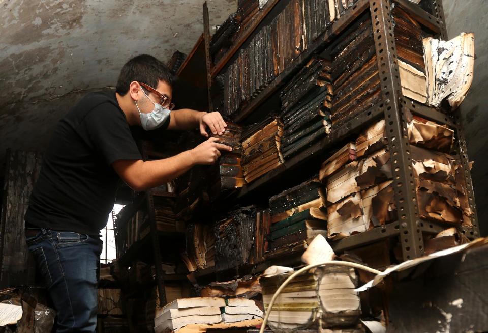 In this picture taken on Sunday, Jan. 5, 2014, a Lebanese activist removes burned books, at the Saeh (Tourist) Library which was set on fire by masked men, in the northern city of Tripoli, Lebanon. Books that were burnt in an arson attack targeting a crammed, chaotic and popular library in the northern Lebanese city of Tripoli have become the latest victim of the country's rising sectarian tensions.(AP Photo/Hussein Malla)