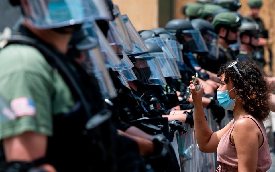 A protester shows a picture of George Floyd from her cell phone to a wall of security guards as she and others demonstrate his death near the White House on June 3, 2020 - AFP