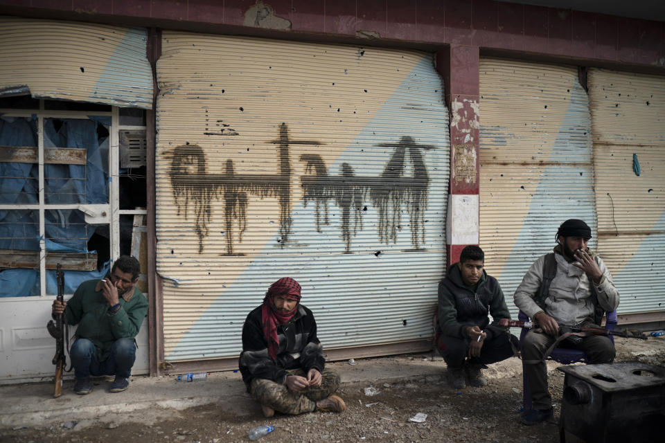 U.S.-backed Syrian Democratic Forces (SDF) fighters sit outside a building as fight against Islamic State militants continue in the village of Baghouz, Syria, Saturday, Feb. 16, 2019. (AP Photo/Felipe Dana)