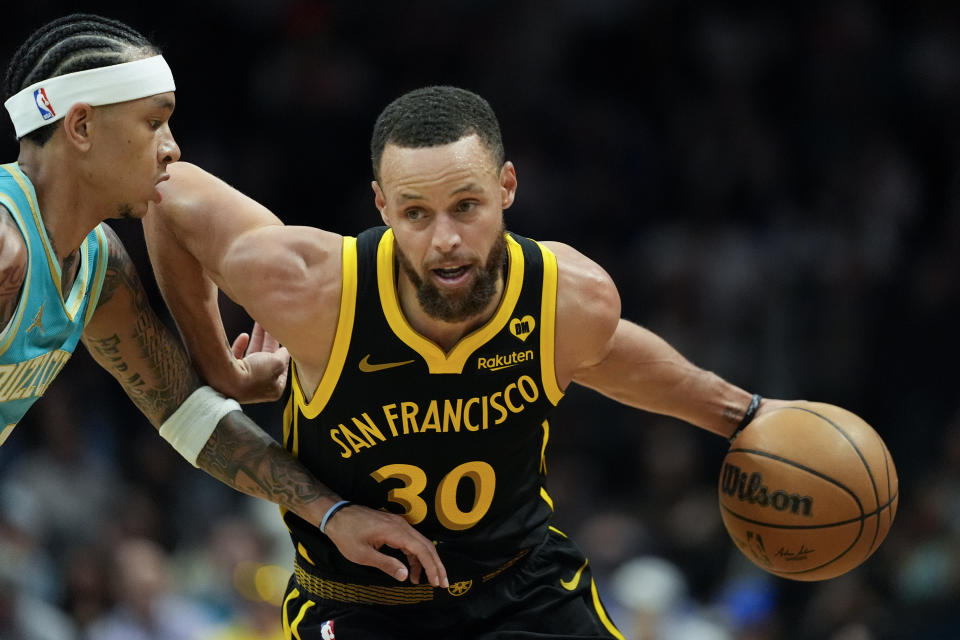 Golden State Warriors guard Stephen Curry drives to the basket past Charlotte Hornets guard Tre Mann during the first half of an NBA basketball game on Friday, March 29, 2024, in Charlotte, N.C. (AP Photo/Chris Carlson)