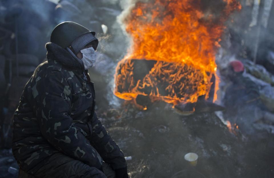 An opposition supporter sits next to a burning tire at a barricade in central Kiev, Ukraine, Thursday, Jan. 30, 2014. Ukraine's embattled president Viktor Yanukovych is taking sick leave as the country's political crisis continues without signs of resolution. (AP Photo/Darko Bandic)