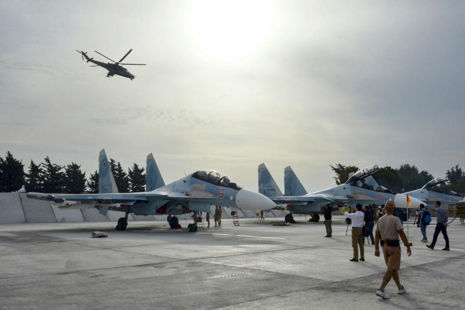 FILE - Journalists film Su-30 jets parked at Hemeimeem airbase, Syria, on Oct. 22, 2015, as Mi 24 helicopter gunship flies overhead. Russia begins airstrikes in Syria, which Putin calls necessary to destroy terrorist groups. The action helps Syrian President Bashar Assad, a longtime ally, remain in power. (AP Photo/Vladimir Kondrashov, File)