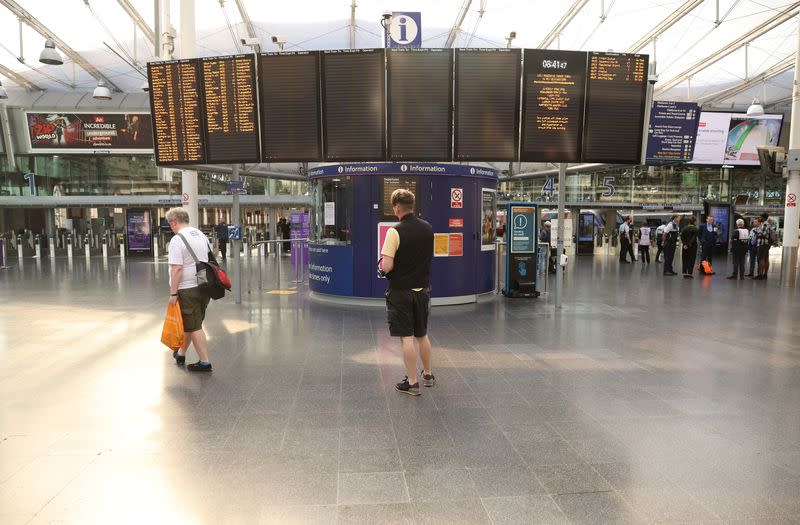 FILE PHOTO: People stand in front of an empty information board on the first day of a national rail strike at Manchester Piccadilly Station in Manchester