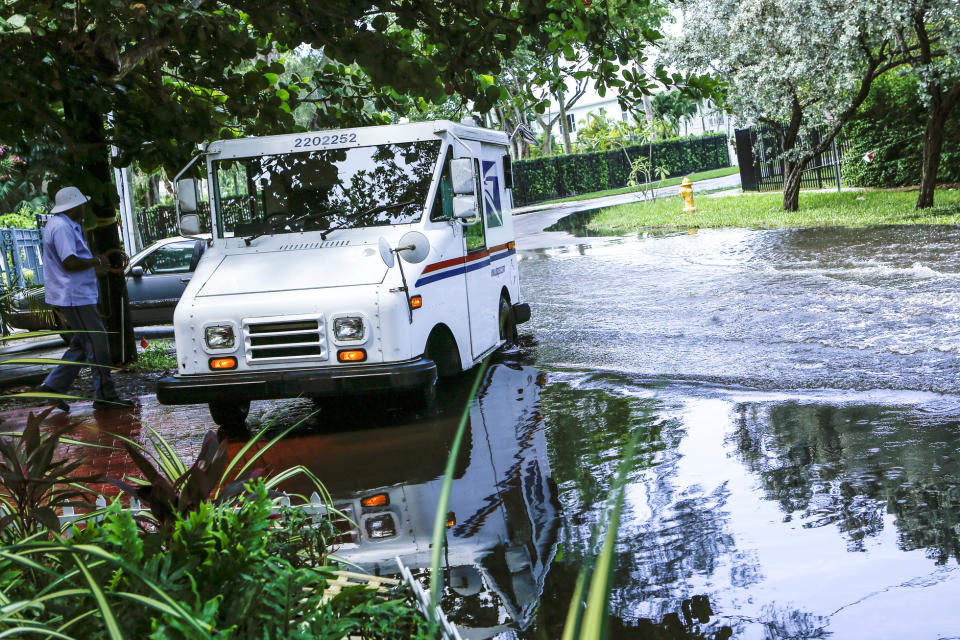 In this Wednesday, June 19, 2019 photo, a postal worker returns to their truck parked on a flooded street a few miles from the downtown Miami venue where the first Democratic presidential debate will be held. Some consider Miami the Ground Zero for any climate-related sea level rise in the United States. Many local residents and coastal community leaders will be listening for any proposals to stave off the effects of rising seas. (AP Photo/Ellis Rua)