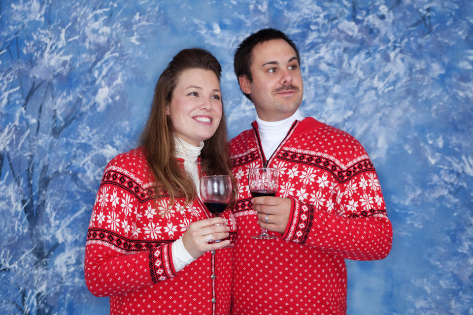 Two people in matching festive sweaters holding wine glasses