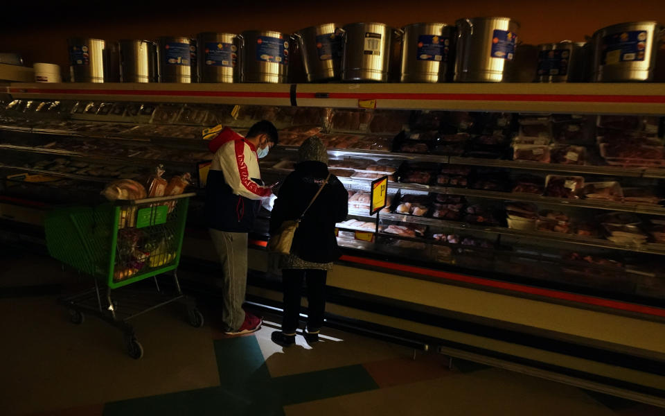 FILE - Customers use the light from a cell phone to look in the meat section of a grocery store Tuesday, Feb. 16, 2021, in Dallas. Even though the store lost power, it was open for cash only sales. A series of winter storms and widespread power outages gripping Texas and other states not used to such extreme low temperatures are creating big challenges in the nation’s food supply networks.(AP Photo/LM Otero)