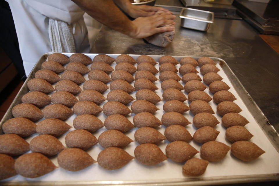 In this June 17, 2019, photo, in preparation for the Refugee Food Festival, chef Diaa Alhanoun rolls out ground meat while preparing kibbeh, in New York, in the kitchen at Porsena, an East Village Italian restaurant hosting Alhanoun for the annual event. A global initiative to help refugees integrate into their adopted communities, the festival takes place in major cities with the goal of introducing refugee chefs and their cuisine to local residents. Kibbeh meatballs are a made of ground beef, bulgur wheat, and onions, seasoned with cinnamon and allspice, formed into a hollow shell for stuffing, then deep fried or baked. (AP Photo/Kathy Willens)