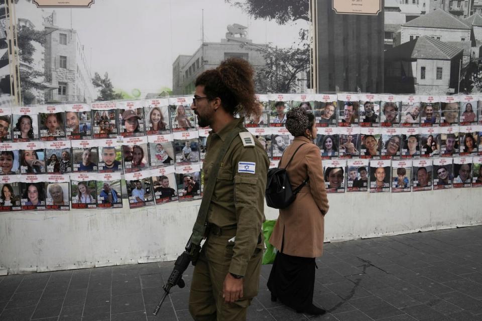 Israelis pass by a wall in Jerusalem with photos of the approximately 240 hostages who were abducted by Hamas on 7 October (AP)