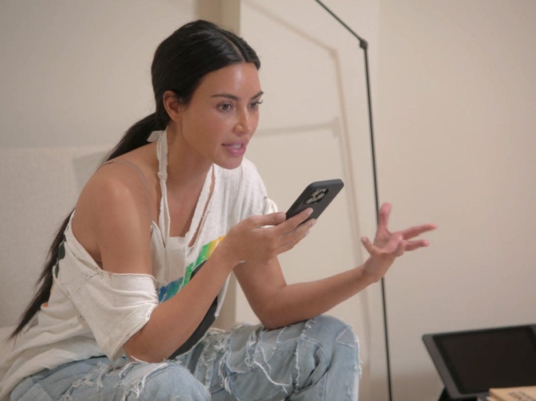 kim kardashian holding her phone, gesticulating widely with her left hand and looking irritated