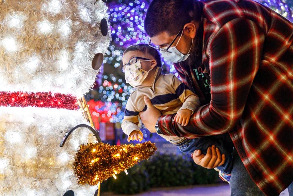 Eric Nolasco holds Gabe while he reaches and looks at his favorite holiday decoration, an upside-down snowman. The Nolascos visited a holiday light exhibit outside of Cook's Children's Medical Center in Fort Worth, Texas on Dec. 2, 2023. Gabe Nolasco, 4, is currently recovering from a thymus transplant as treatment for his congenital athymia. As such, the Nolascos quarantine and wear masks in spaces with other people in order to avoid contamination.