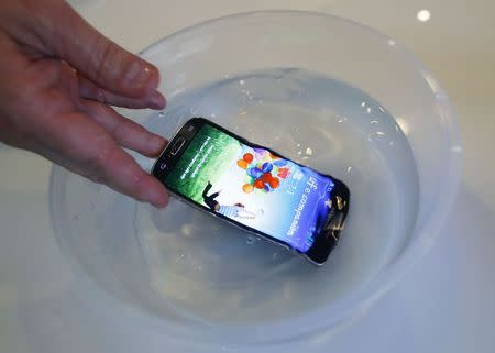 P2i's CEO Carl Francis demonstrates a mobile phone, treated with their thin, transparent, splash-resistant polymer coat, functioning in water, during an interview with Reuters in Singapore July 31, 2014. REUTERS/Edgar Su