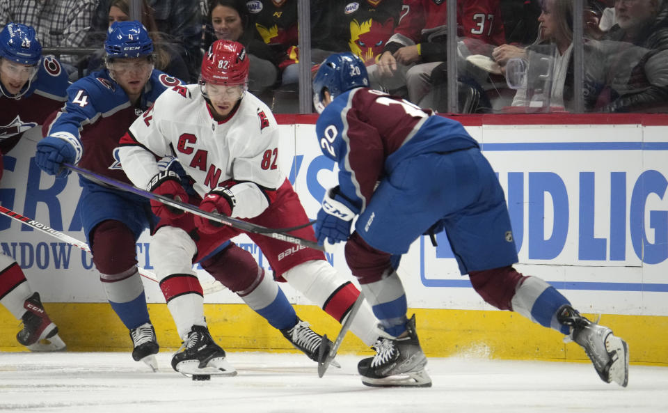Carolina Hurricanes center Jesperi Kotkaniemi (82) fights for control of the puck with Colorado Avalanche defenseman Bowen Byram (4) and center Ross Colton (20) in the third period of an NHL hockey game on Saturday, Oct. 21, 2023, in Denver. (AP Photo/David Zalubowski)