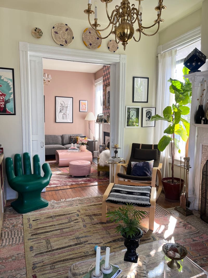 Pink living room seen from yellow record room with corner chair and ottoman and green hand shaped chair.