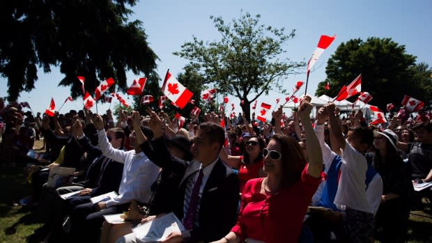 New Canadians wave flags after taking the oath of citizenship during a special Canada Day ceremony in Vancouver on July 1. (Darryl Dyck/Canadian Press)