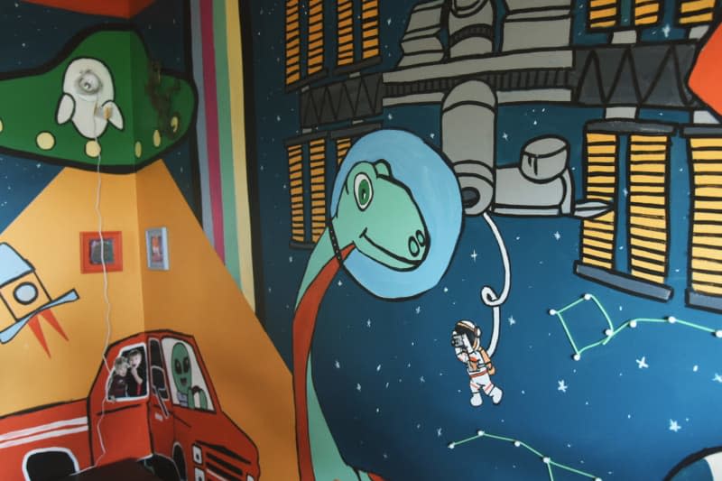 kids room with colorful space and dinosaur themed painted walls and ceiling